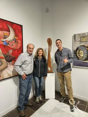 Tres personas junto a una escultura en una exposición