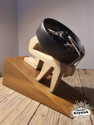 Escultura oscura de madera y metal, con una forma circular sostenida sobre una base geométrica