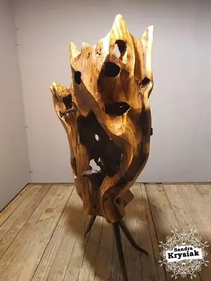 Escultura orgánica de madera y metal, con huecos y vetas visibles, fotografiada en una exposición
