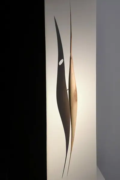 Dos formas de madera afiladas, iluminadas sobre fondo blanco, en una sala de exposición