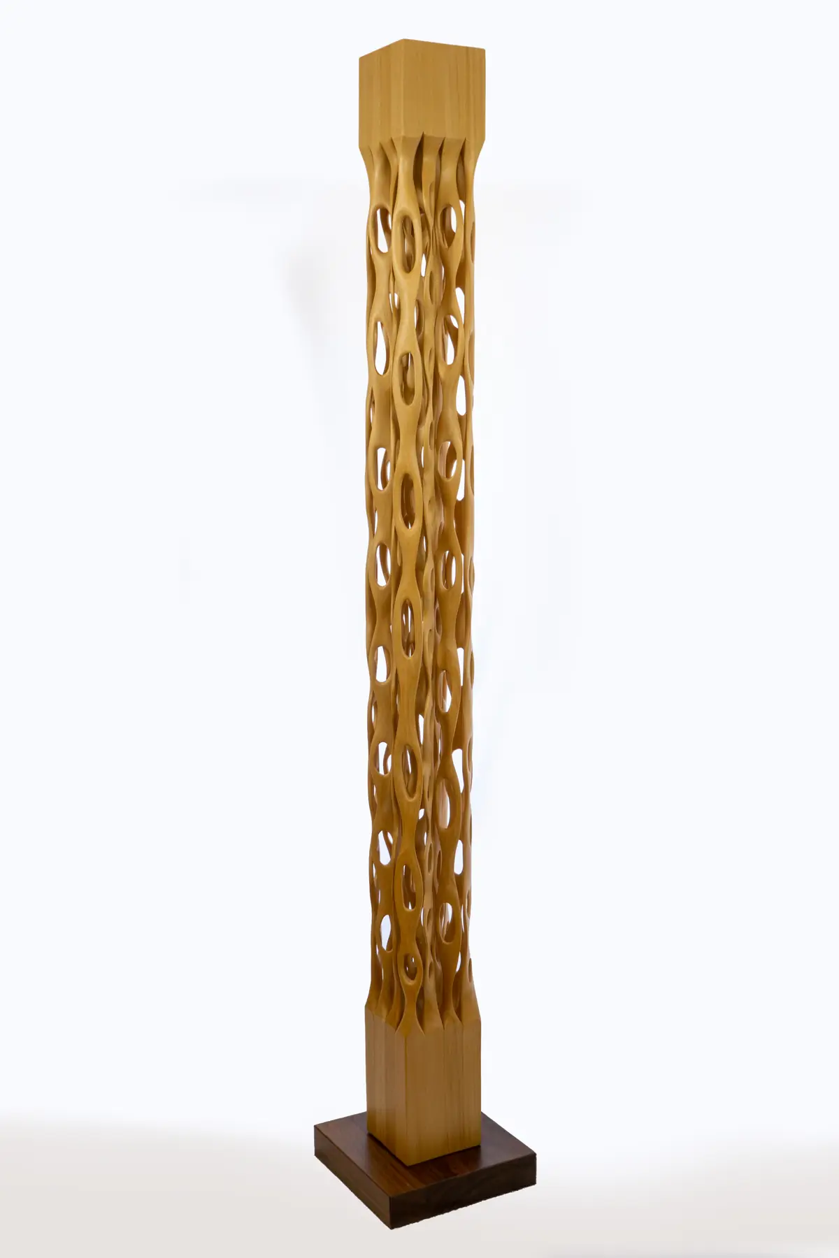 Columna vertical de ayous calada con vacíos ovalados encadenados, sobre una peana cuadrada de madera oscura