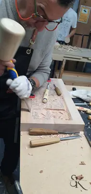 Manos con guantes tallando un panel sujeto al banco