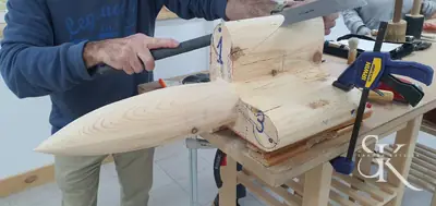 Manos tallando un bloque de madera sujeto al banco del taller