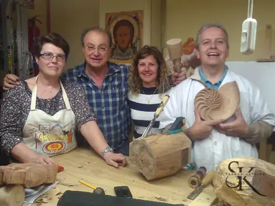 Cuatro alumnos junto al banco de trabajo; uno muestra una talla circular de madera