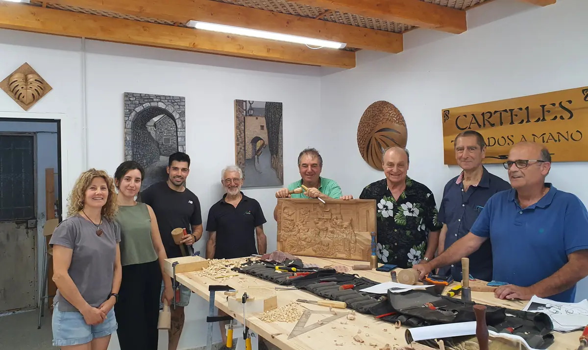 Grupo de alumnos sonrientes junto a la mesa del taller, con herramientas y un relieve de madera terminado