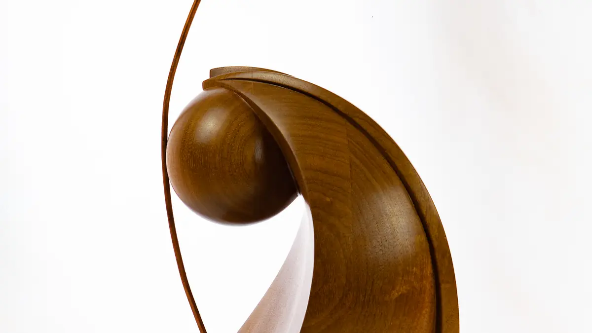 Escultura de madera de sipo con una forma envolvente y una esfera, atravesada por un arco fino de acero