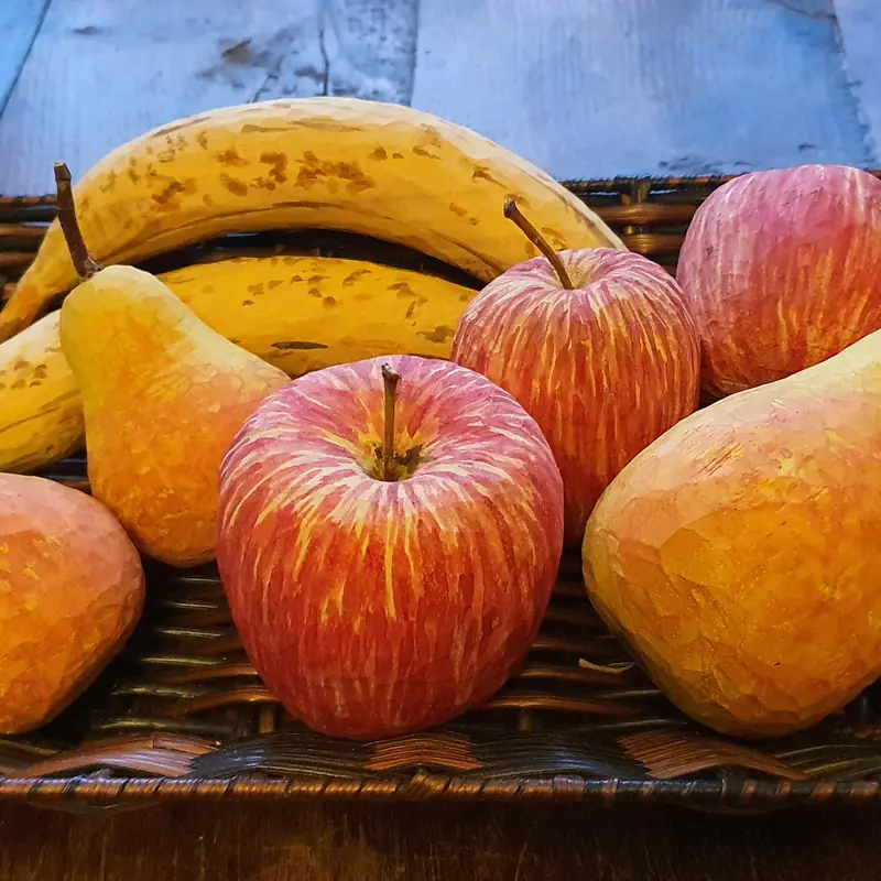 Peras, manzanas y un plátano tallados en madera y pintados, en una bandeja de mimbre
